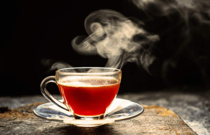 湯気が立ちのぼる紅茶の入ったガラスのティーカップとソーサー。背景は暗く、温かい雰囲気が強調されている。
